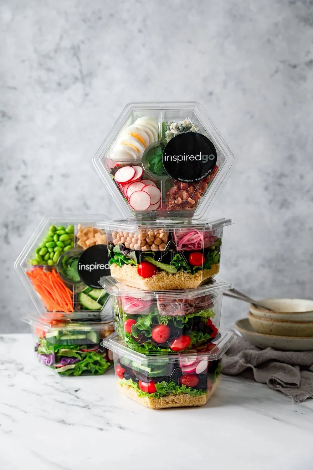 A stack of sealed InspiredGo ready-to-eat salad packages: five fresh lunches ready for the week
