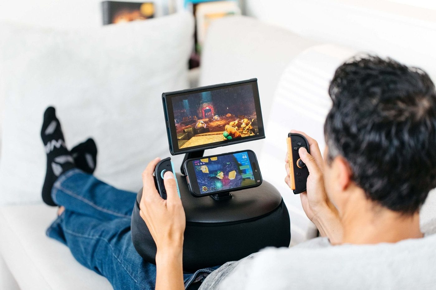 Person on a couch playing a Switch 2 in a Basecase, mounted on the Mechanism Gaming Pillow with a phone as a second screen
