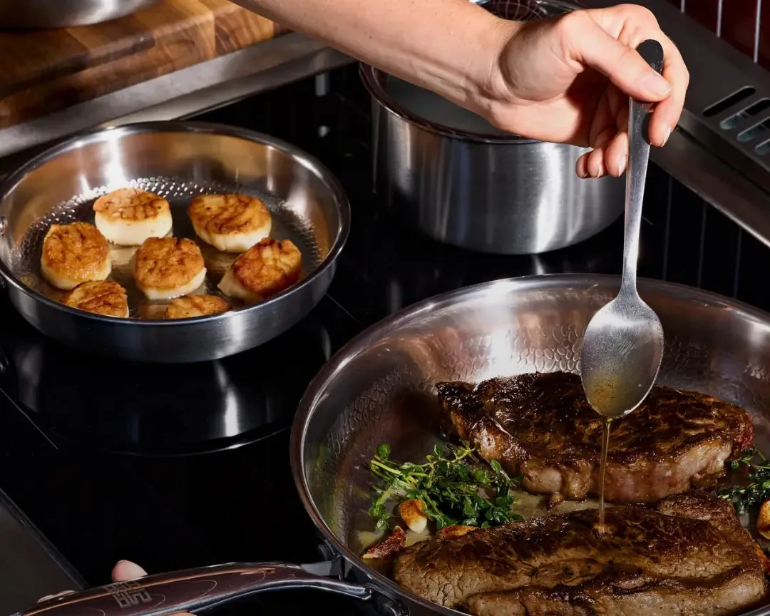 Steak and scallops searing in Siraat titanium hammered pans on the stove